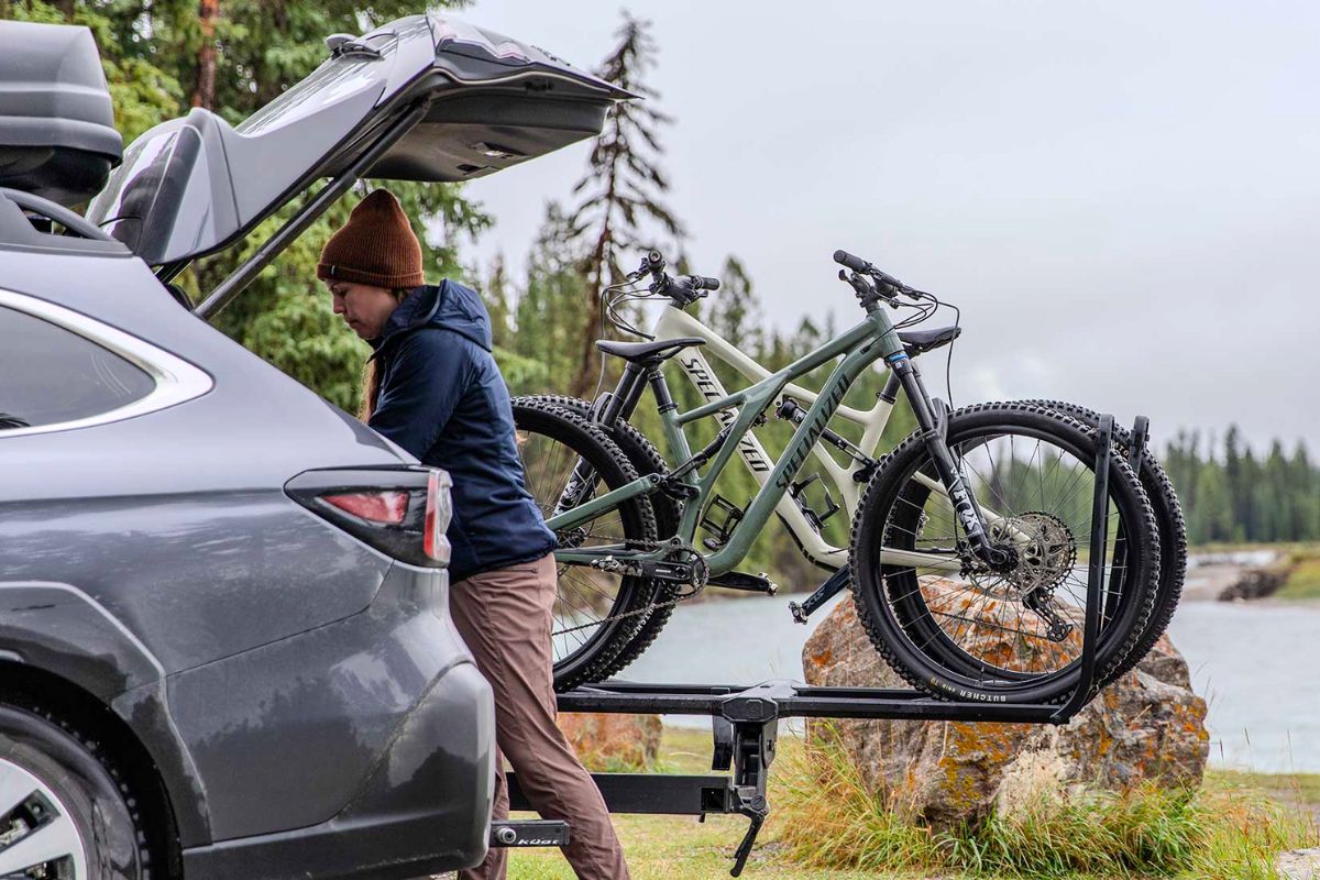 Woman accessing Subaru Outback cargo area with mountain bikes on a Kuat Pivot v2 swing-away rack