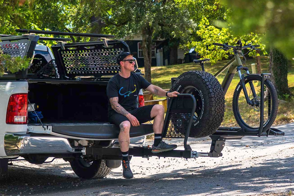 Man sitting on pickup truck tailgate with Kuat Pivot XD swing-out spare tire bike carrier