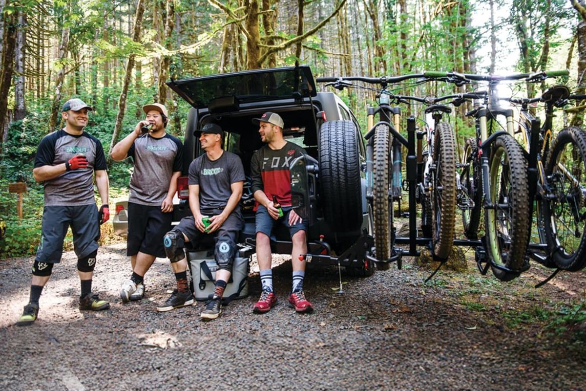 Four mountain bikers relaxing by a Jeep Wrangler with a Yakima BackSwing adapter holding bikes